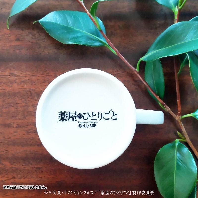 藥師少女的獨語美濃燒馬克杯，俯視圖，白色杯身印有黑色標誌，木質桌面搭配綠葉。